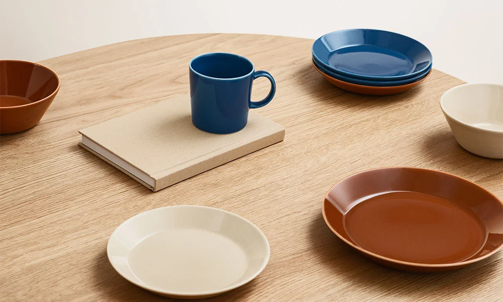 Iittala Teema Keramikgeschirr, darunter Teller, Schalen und Tassen, arrangiert auf einem Holztisch in minimalistischer Ästhetik.