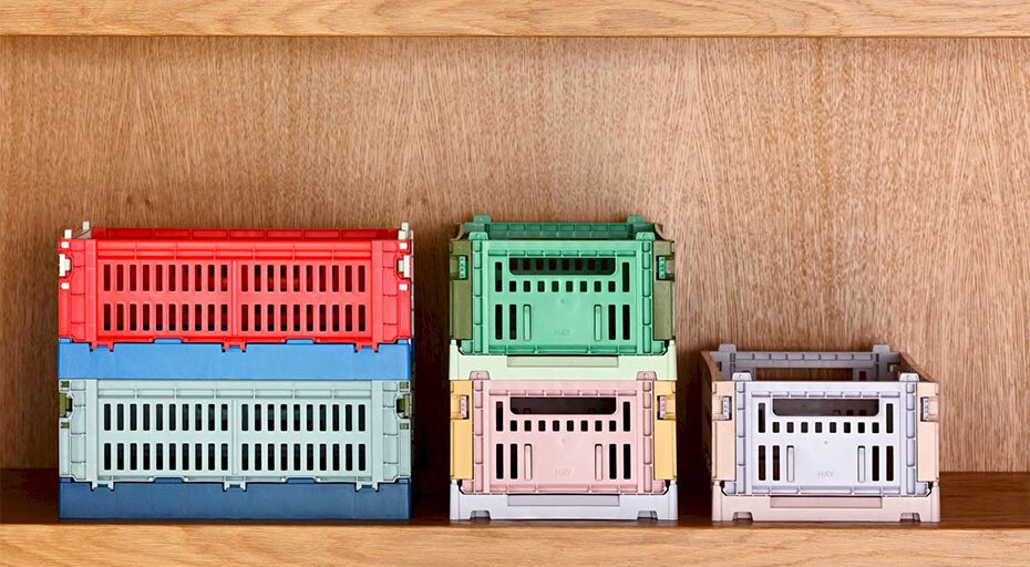 Verschiedene farbige Stapelboxen aus Kunststoff von Hay, ordentlich auf einem Holzregal angeordnet.