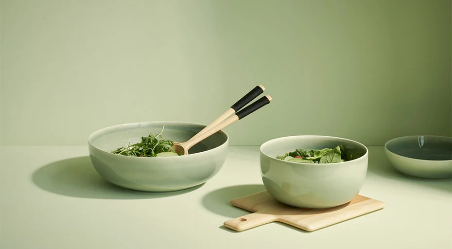 Zwei Schüsseln der Serie Saisons Agave von ASA mit Salat auf einem Tisch, eine Schüssel hat Holzsalatbesteck, grüne Farbpalette.