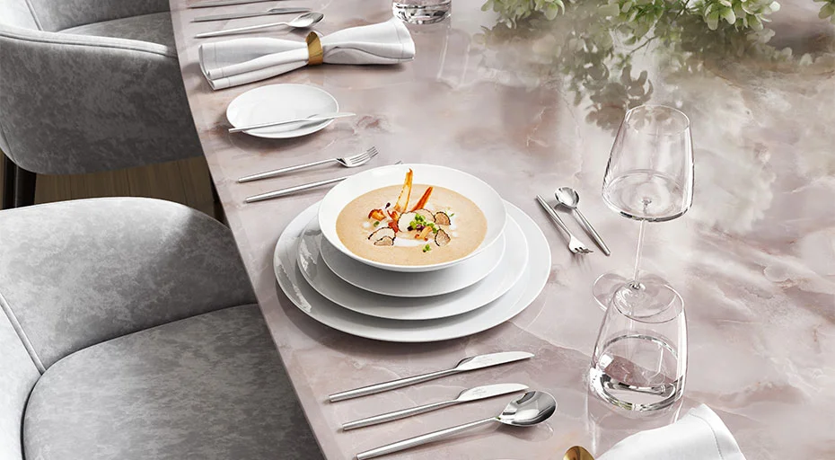Elegante Tischdekoration mit Suppenteller, Besteck, Gläsern und Blumenarrangement auf einem polierten Marmortisch.