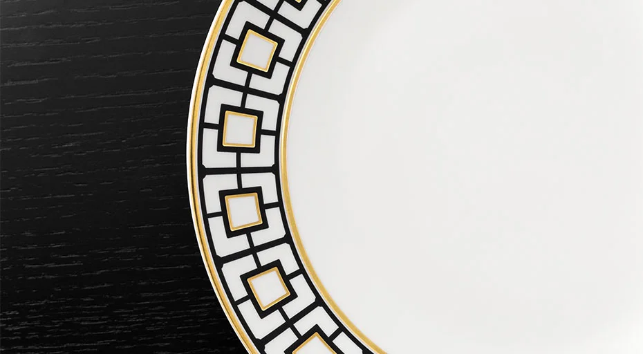 Porzellanteller der Serie MetroChic von Villeroy &amp; Boch mit geometrischem Muster und goldenen Akzenten auf schwarzem Hintergrund, teilweise sichtbar.