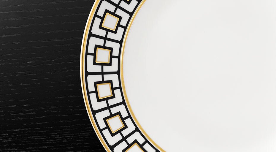 Porzellanteller der Serie MetroChic von Villeroy &amp; Boch mit geometrischem Muster und goldenen Akzenten auf schwarzem Hintergrund, teilweise sichtbar.