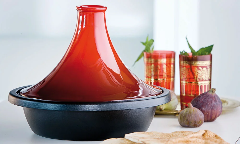 Rote Le Creuset Tajine mit schwarzem Boden, neben Teegläsern und Feigen auf einem Tablett.