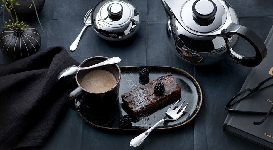 Elegantes Kaffeeservice mit Teekanne, Tasse, Besteck von Robbe &amp; Berking und Schokoladendessert auf dunkler Tischdecke.