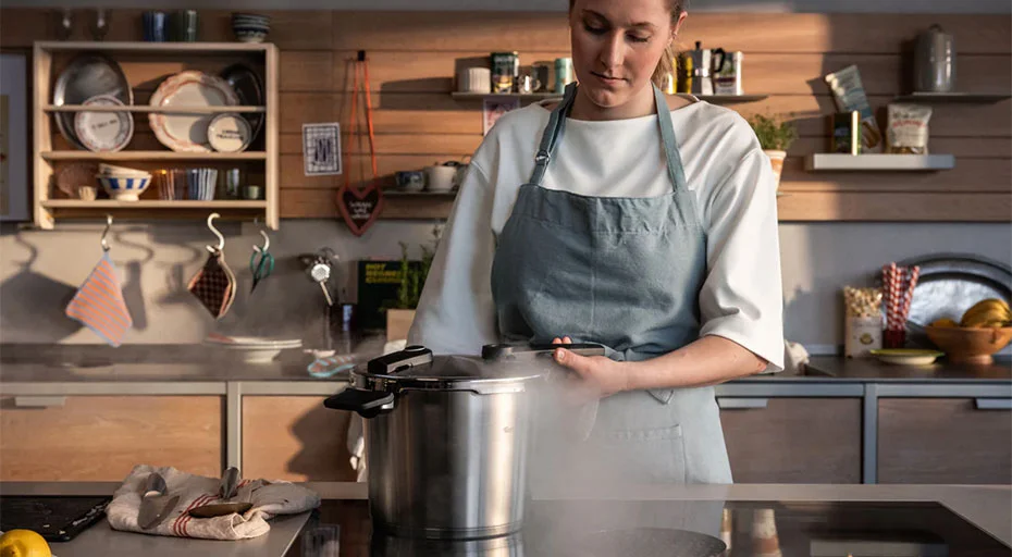 Person kocht mit einem Fissler Schnellkochtopf in moderner Küche, Dampf steigt auf. Küchenutensilien und Geschirr im Hintergrund.