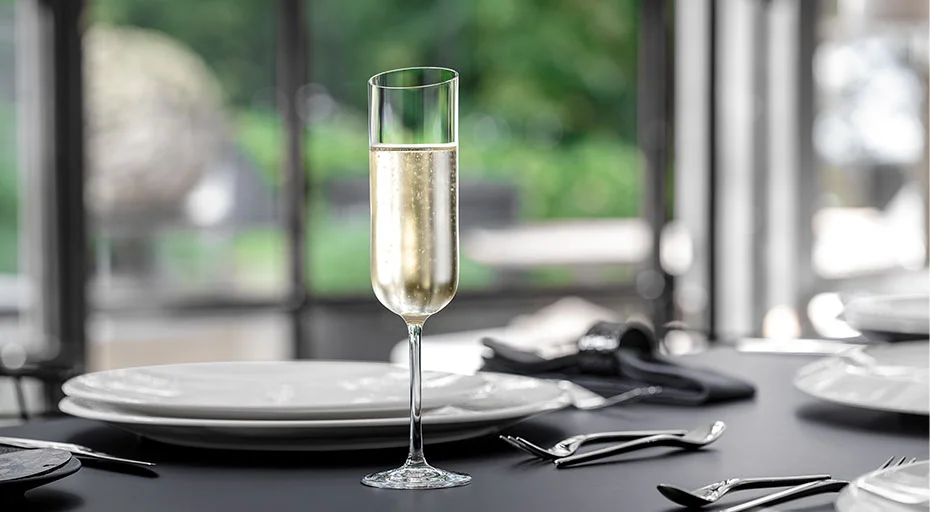 Champagnerflöte von Villeroy &amp; Boch mit Schaumwein auf gedecktem Tisch, Hintergrund unscharf mit grünem Garten.
