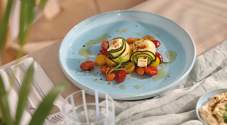 Zucchini-Röllchen und Tomaten auf blauem Teller der Serie Perlemor Aqua von Villeroy &amp; Boch angerichtet, dekorativ mit Öl beträufelt.