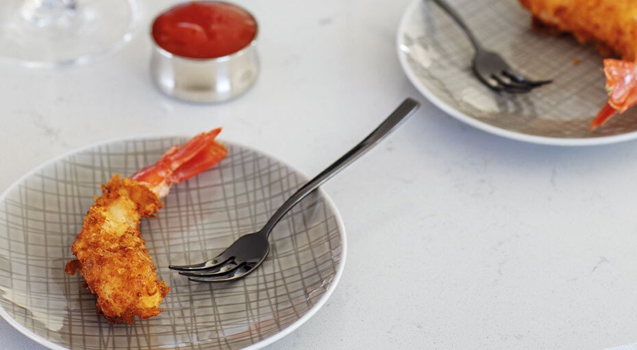 Gebackene Garnelen auf grauen Tellern mit schwarzen Gabeln und Schälchen mit roter Soße im Hintergrund.