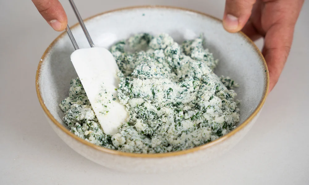 Schüssel mit Ricotta und Spinat, die mit einem Spatel vermengt werden.