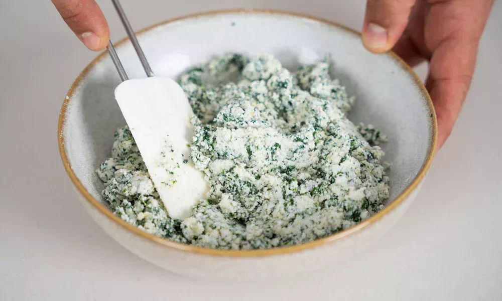 Schüssel mit Ricotta und Spinat, die mit einem Spatel vermengt werden.