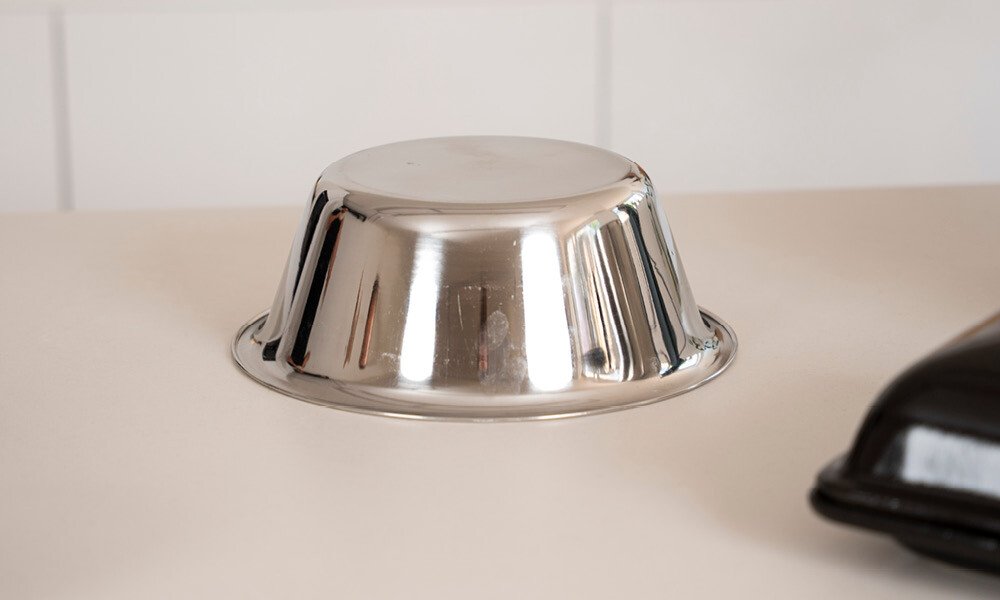 Eine umgedrehte Edelstahlschüssel auf einer weißen Oberfläche.