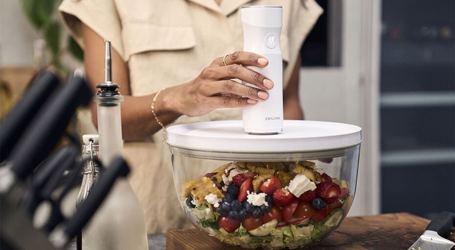 Person vakuumiert eine Schüssel mit gemischtem Salat und Obst, indem ein Vakuumgerät auf dem Deckel verwendet wird.