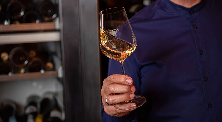 Person hält ein Glas der Serie Kolibri von Zwiesel Glas, befüllt mit Weißwein in einer Weinkellerei.