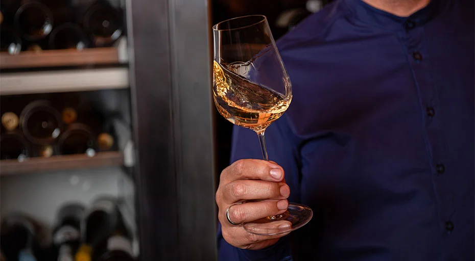 Person hält ein Glas der Serie Kolibri von Zwiesel Glas, befüllt mit Weißwein in einer Weinkellerei.