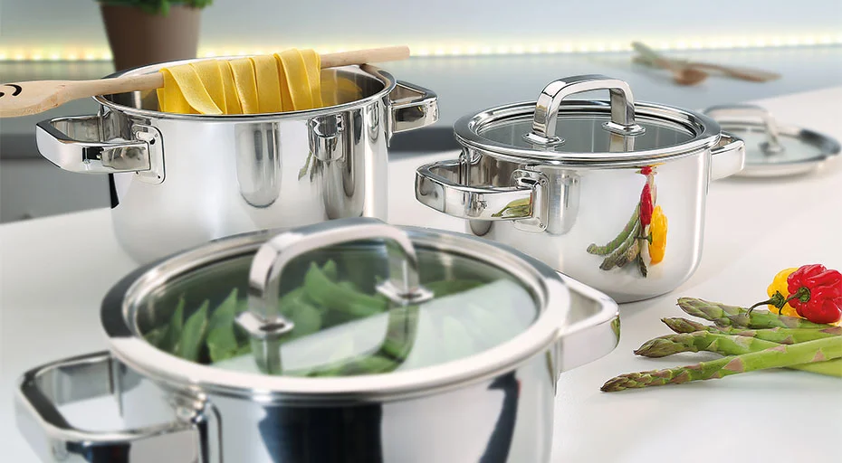 Drei Töpfe mit Glasdeckeln, gefüllt mit Pasta und Gemüse, auf weißer Küchenarbeitsfläche.