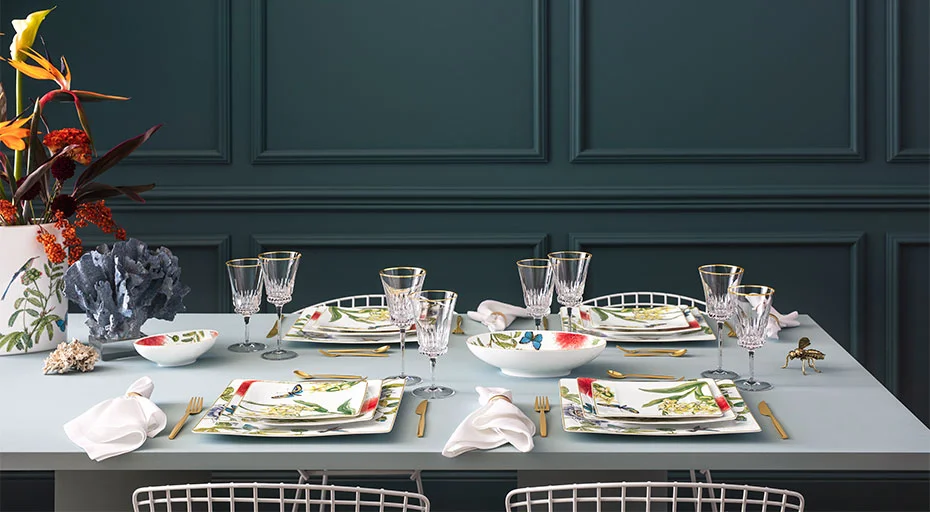 Eleganter Esstisch mit floralem Geschirr der Serie Amazonia Anmut von Villeroy &amp; Boch, Kristallgläsern, goldenen Bestecken und dekorativen Blumenarrangements.