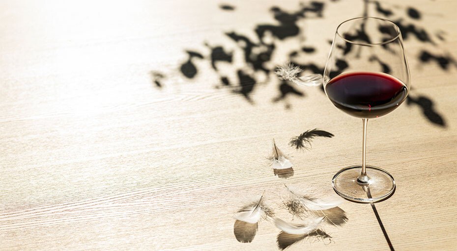 Rotweinglas Vuelo von Zwiesel Glas auf einem Tisch mit Schatten von Blättern und dekorativen Federn.