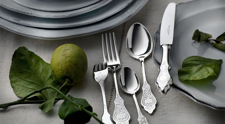 Silberbesteck der Serie Ostfriesen von Robbe &amp; Berking mit kunstvollem Design neben einem Teller und einer Limette auf einem Tisch.