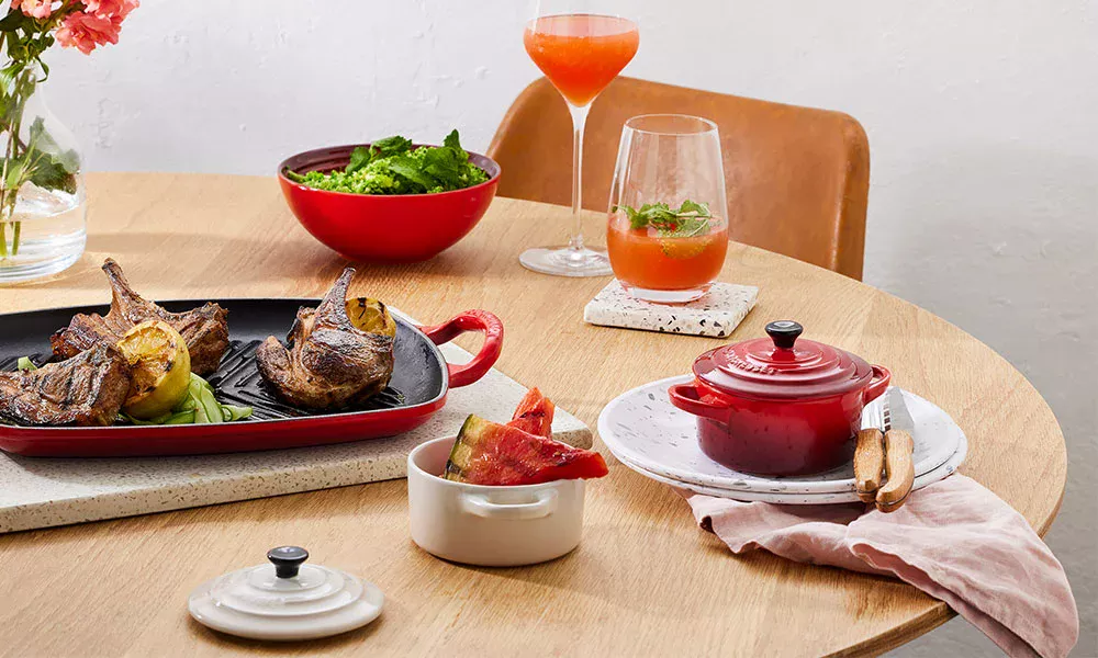 Runder Holztisch mit geröstetem Gemüse, Salatschüssel, Getränken und roten Keramiktöpfen, dekorativ arrangiert.