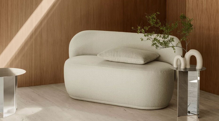 Modernes Sofa in cremefarbenem Stoff, mit Kissen, neben einem Tisch mit Pflanzenarrangement und Vasen von Blomus, vor holzverkleideter Wand.