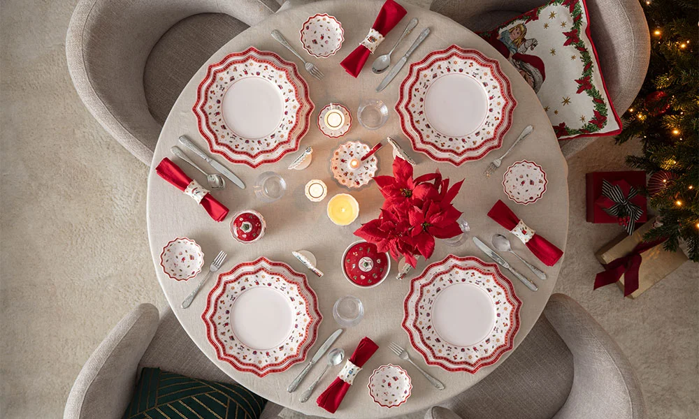 Festlich gedeckter Tisch mit rotem Geschirr der Serie Toy's Delight von Villeroy &amp; Boch, Kerzen und weihnachtlicher Dekoration aus Vogelperspektive.