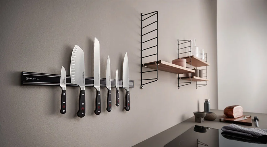 Moderne Küche mit magnetischer Messerleiste, darauf diverse Messer von Wüsthof. Im Hintergrund hängende Regale mit Gläsern und Gewürzbehälter.