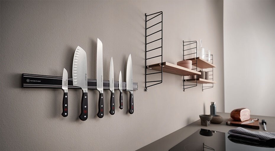Moderne Küche mit magnetischer Messerleiste, darauf diverse Messer von Wüsthof. Im Hintergrund hängende Regale mit Gläsern und Gewürzbehälter.