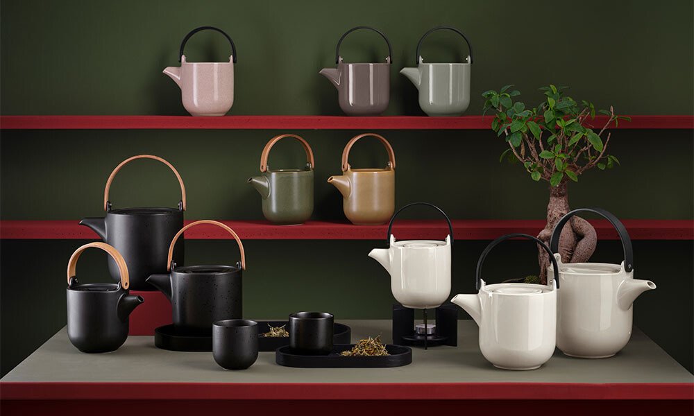 Elegante Teekannen der Serie ASA Coppa und Tassen in neutralen Farben auf roten Regalen, akzentuiert durch eine Pflanze in einem minimalistischen Design.