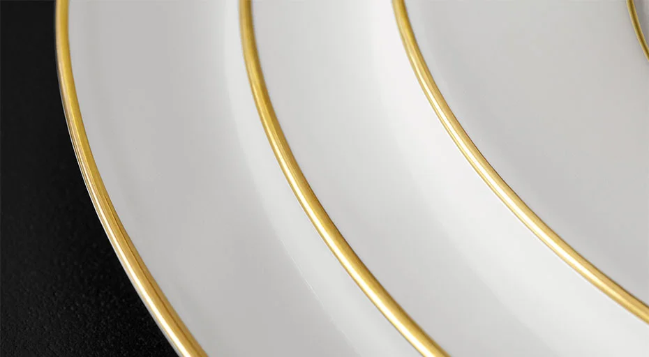 Weiße Porzellanteller der Serie Anmut Gold von Villeroy &amp; Boch mit goldenen Rändern, übereinander gestapelt, auf schwarzem Untergrund.