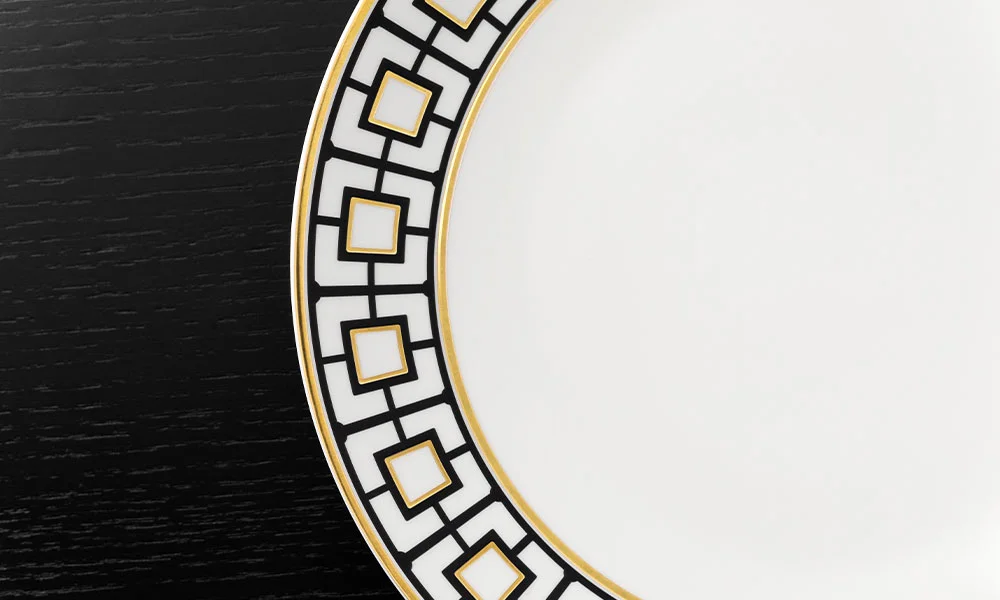 Nahaufnahme eines Tellers mit geometrischem Muster in Schwarz und Gold auf dunklem Holzuntergrund.