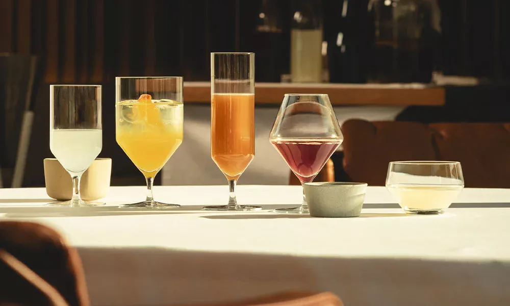 Fünf stilvolle Getränkegläser der Serie Début von Zwiesel Glas mit unterschiedlichen Getränken und Mocktails, auf einem Tisch in elegantem Ambiente platziert.