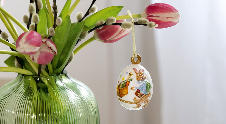 Glasvase mit blühenden Tulpen, daran hängt ein bemaltes Jahresei der Annual Easter Edition von Villeroy &amp; Boch mit Hasenmotiv.