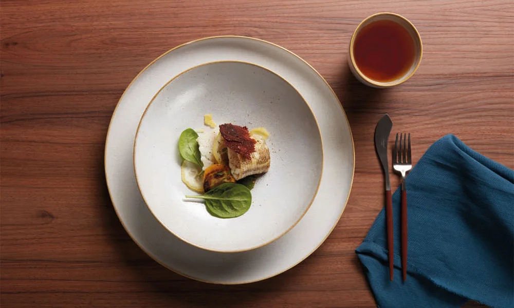 Gourmetgericht mit Fischfilet, Spinat, knusprigem Topping, Beilage, auf weißem Teller, daneben eine Tasse Tee.