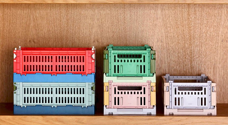 Verschiedene stapelbare Kisten von HAY in Rot, Blau, Grün und Beige auf einem Holzregal.