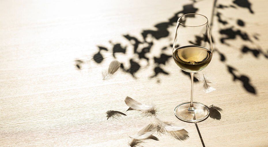 Weißweinglas Vuelo von Zwiesel Glas auf einem Tisch mit Schatten von Blättern und dekorativen Federn.