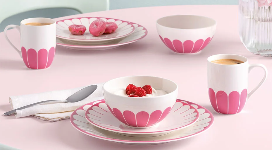 Teller, Tassen und Schalen von Villeroy &amp; Boch Fleur Cassis in Weiß und Rosa, gefüllt mit Kaffee, Joghurt und Himbeeren; daneben liegen Muffins und Besteck.
