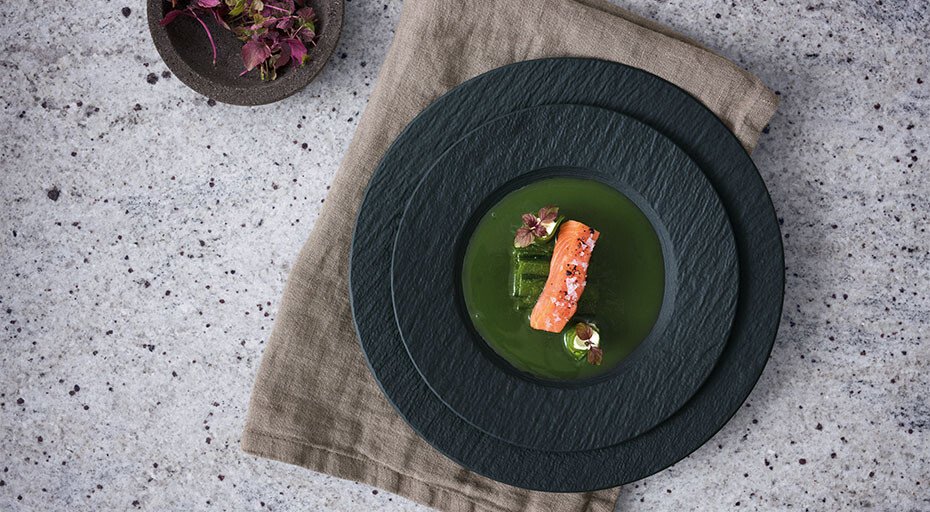 Gourmetgericht mit Lachsfilet und grüner Sauce, kunstvoll auf schwarzen Tellern der Serie Manufacture Rock von Villeroy &amp; Boch neben beiger Stoffserviette.