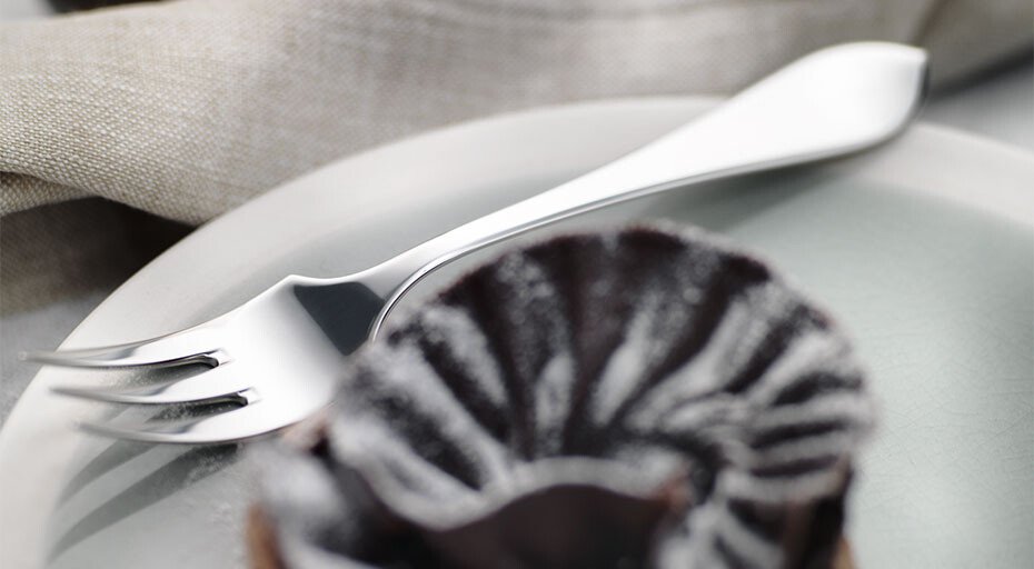 Dessert-Gabel der Serie Eclipse von Robbe &amp; Berking neben einem Schokoladenkuchen mit Puderzucker auf einem Teller.