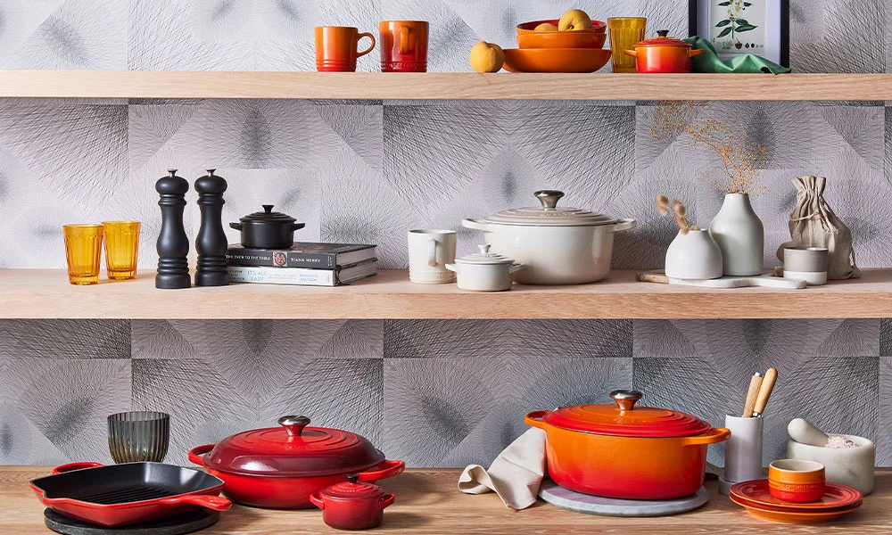 Küchenregale mit buntem Keramikgeschirr, Töpfen und Gewürzmühlen, von Le Creuset dekoriert mit Büchern, Vasen und Objekten aus Naturmaterialien.