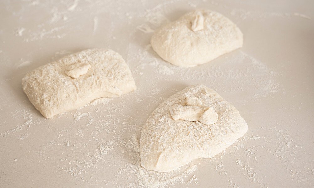 Drei bemehlte Teigstücke auf einer Backfläche, bereit zum Weiterverarbeiten.
