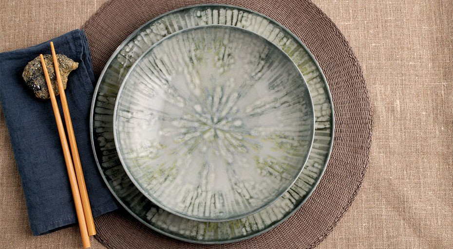 Rosenthal Arthur Krupp Keramikteller auf braunem Platzdeckchen, daneben Holzstäbchen auf dunkelblauer Serviette.