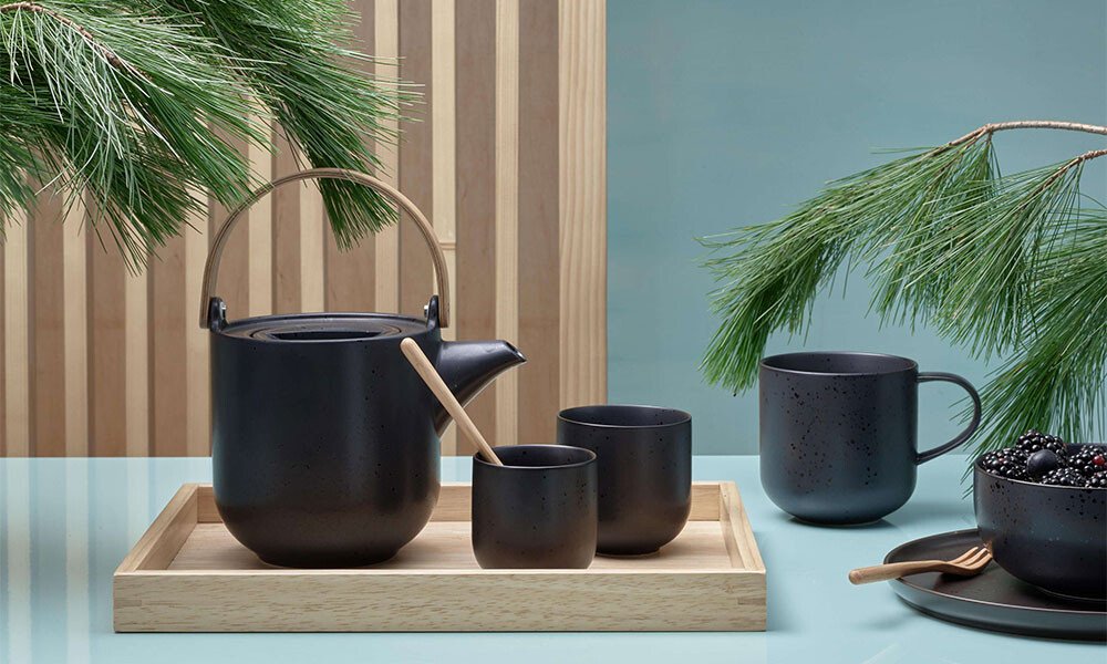 Teekanne und Tassen von ASA Coppa Kuro auf Tablett, umgeben von Kiefernzweigen. Elegant arrangierte, moderne Teeservice-Komposition.