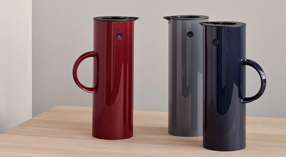 Drei Stelton Isolierkannen in Rot, Grau und Blau auf einem Holzuntergrund.
