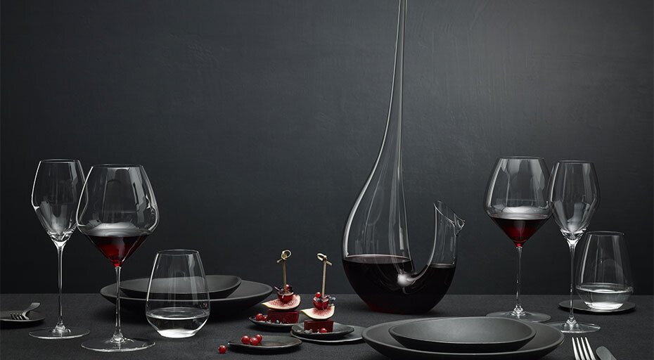 Elegante Tischdekoration mit Weingläsern der Serie Veloce von Riedel, Dekanter und schwarzen Tellern, verziert mit roten Beeren und Feigen.