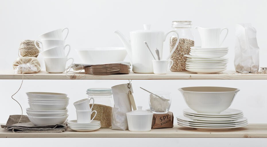 Weißes Geschirr der Serie Jade weiß von Rosenthal und diverse Küchenutensilien auf Regalen arrangiert, umgeben von Naturmaterialien wie Juteschnur und Stoff.