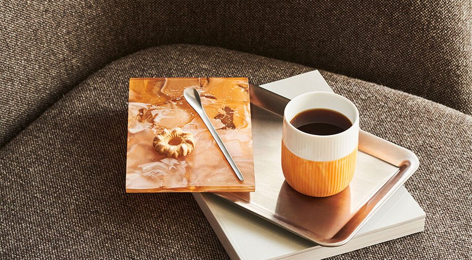 Tasse Kaffee von Royal Copenhagen auf Tablett mit Buch und Notizheft auf Sofa platziert.