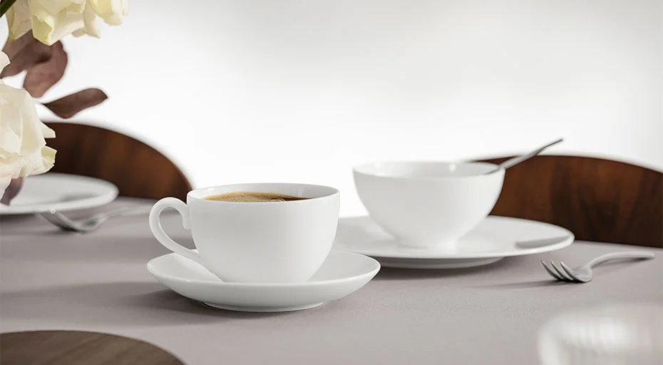 Kaffeetasse aus Fine Bone China und Schale auf gedecktem Tisch mit minimalistischer Dekoration.