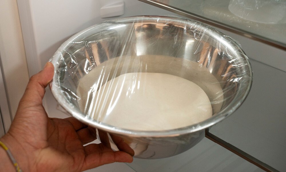 Baguette-Teig in einer mit Frischhaltefolie abgedeckten Metallschüssel im Kühlschrank.