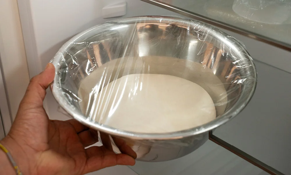Baguette-Teig in einer mit Frischhaltefolie abgedeckten Metallschüssel im Kühlschrank.