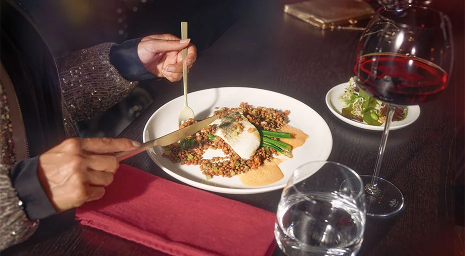Person speist in einem gehobenen Restaurant: Teller der Serie Jade Lift von Rosenthal mit Fisch, Linsen, Gemüse; dazu Rotwein und Wasser.
